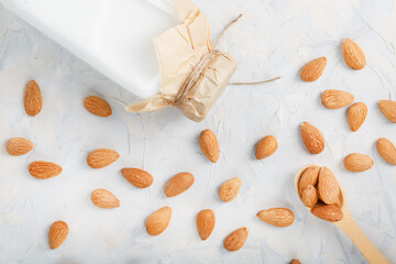 Almond milk in a glass bottle on a light background with a scattering of seed kernels and a wooden spoon.