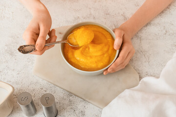 Woman eating tasty pumpkin cream soup on light background