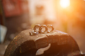Freshly machined stainless steel nuts sit in a vise against the backdrop of sunlight.