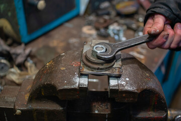 The locksmith tightens the nut on the fixture clamped in a vice with a wrench. Industrial composition