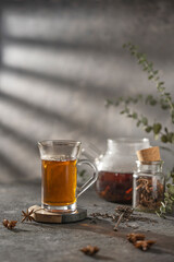 hot tea in glass cap, beautiful gray textured table with dry spices and transparent teapot,  Studio shot with copy space.