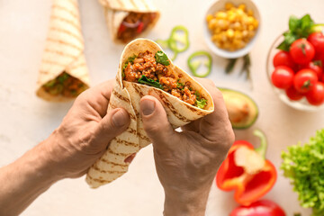 Man holding tasty burrito on light background, closeup