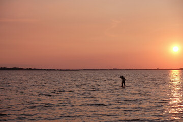 Fototapeta premium Silhouette of a lonely man in the water. Calming coral color sunset background. Svityaz lake, Ukraine. 