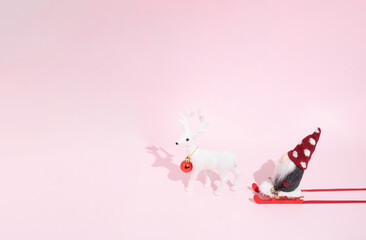 Christmas composition on a pastel pink background. Santa on a red sled and one white reindeer, red decoracion bauble. Xmas and winter  creative idea. Happy New Year 2022