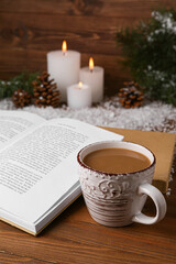 Cup of tasty coffee, book and Christmas decor on wooden background