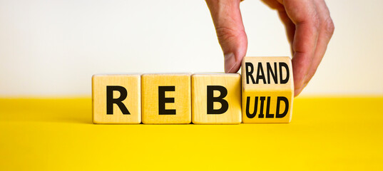 Rebrand and rebuild symbol. Businessman turnsa wooden cubes and changes the word rebrand to rebuild. Beautiful yellow table, white background. Business rebrand and rebuild concept. Copy space.