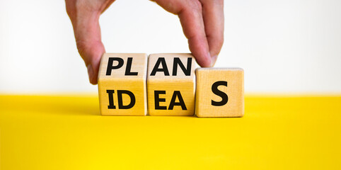 Ideas and plans symbol. Businessman turns wooden cubes and changes the word plans to ideas. Beautiful yellow table, white background, copy space. Business idea and plan concept.