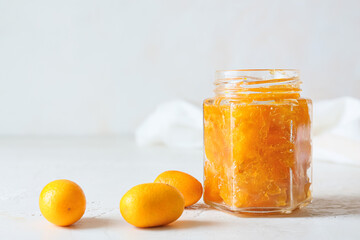 Jar of tasty kumquat jam and fresh fruits on light background