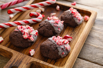 Board with tasty candy cane cookies on wooden background, closeup