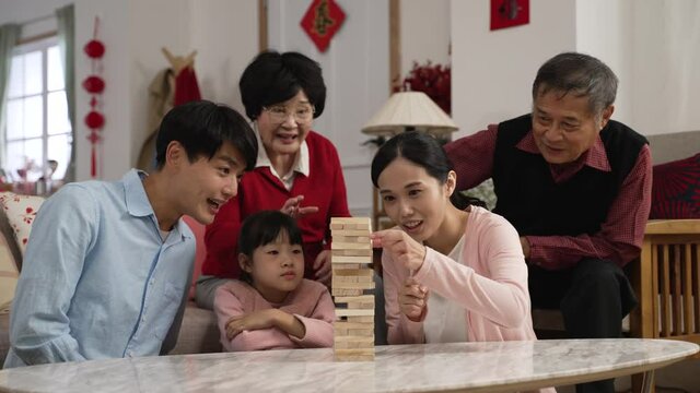 family members laughing at young mother as she makes the tower fall. big family enjoying toy block game during spring festival. word at background translation: spring and happiness