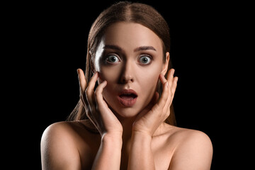 Portrait of shocked young woman on black background
