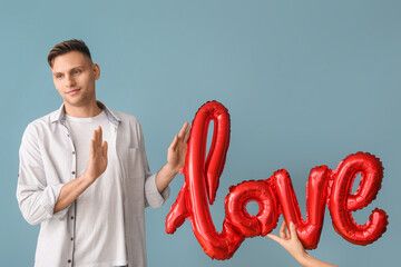 Displeased man refusing balloon in shape of word LOVE on color background