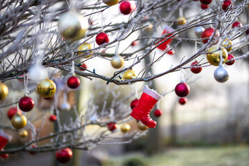 Stiefel und Christbaumkugeln hängen im Winter als Deko im Garten an Büschen und Bäumen