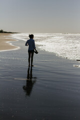 Mujer latina delgada caminando en la playa con sandalias en las manos