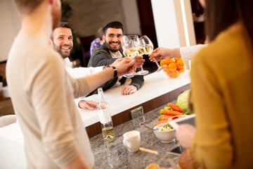 Group of young people preparing meal, drinking white wine and having a good time