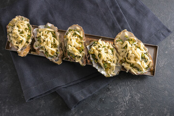 Prepared oysters with herb crust and cheese ready for baking in the oven, dark gray slate...