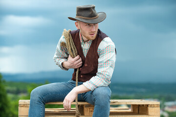 Portrait of farmer or cowboy outdoor. Cowboy with lasso rope on sky background.