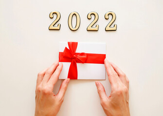 Close-up of metal numbers 2022 and hand on white background holding gift certificate discount voucher. Christmas and New Year presents concept.
