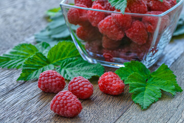 fresh juicy raspberries with green leaves in a plate on a wooden table.