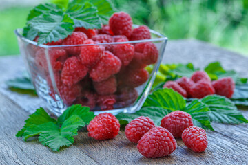 fresh juicy raspberries with green leaves in a plate on a wooden table.