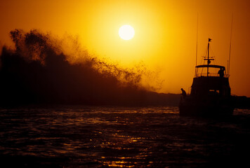 Private boat watches very large wave at breakwater.