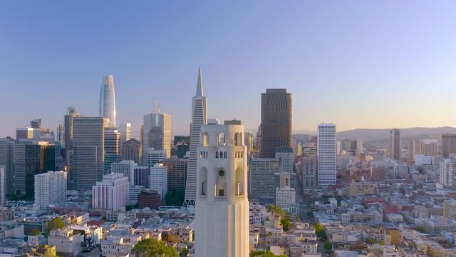 4K aerial video footage of San Francisco, California, at sunset. Movement is over the top of Coit Tower, buildings and houses lit by setting sun, pinkish sky.