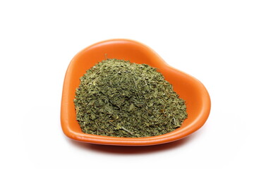 Chopped dry parsley leaves, pile in shape heart, porcelain bowl isolated on white 