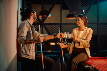 Happy couple toasts with beer while playing snooker in pool hall.