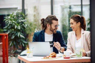 Happy businessman and his female colleague talk while working on laptop in cafe.