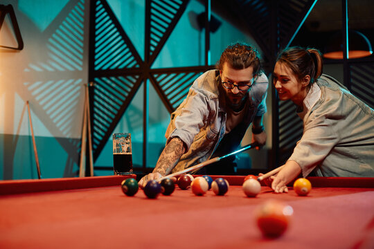 Young man teaches his girlfriend to play billiard in pool hall.
