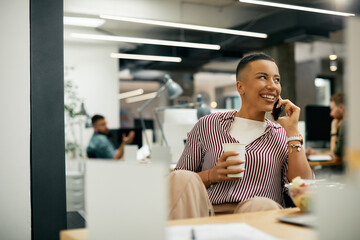 Young black creative woman talks on cell phone while having break at corporate office.