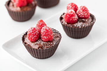 Chocolate raspberry cups topped with fresh raspberries and powdered sugar.