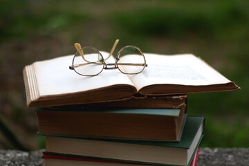 Stack of hardcover books and reading glasses in a garden. Selective focus.