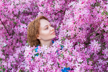 Obraz na płótnie Canvas Portrait of a curly-haired girl on the background of a flowering tree. A girl in pink apple blossoms. The apple tree is in bloom. Spring flowering of the apple orchard.
