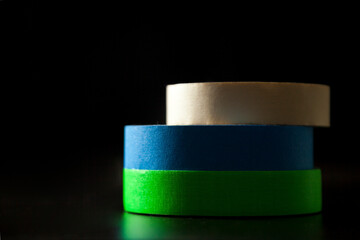 Colored adhesive tapes stacked on a table and black background. With spot light showing the texture. Paper tape, fabric tape and electrical tape. Adhesive tapes concept.
