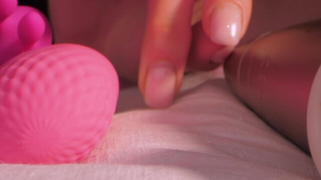 Woman touches clitoris simulator and pink silicone vibrating egg lying on large bed in semi-dark bedroom extreme closeup