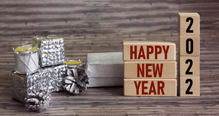 Happy new 2022 year text on wooden blocks, near silver gift boxes on wooden background
