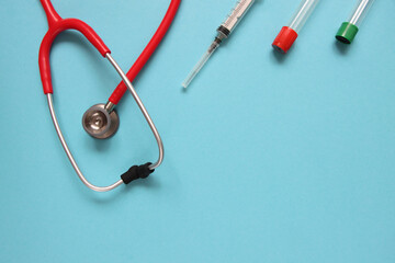 Top view of red stetoscope, syringe, and ampoules on blue background. Medicine concept.