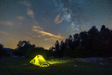 illuminated yellow tent at twilight with milkyway on the sky