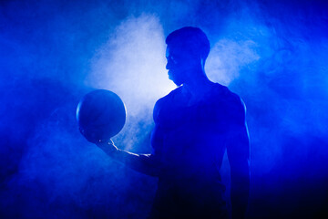 Basketball player holding a ball against blue fog background. African american man silhouette.