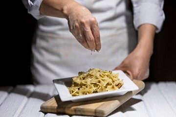 Sprinkling parsley flakes on bowtie pasta.