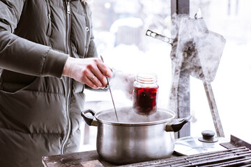young woman in warm jacket pours mulled wine into glass outdoor in winter near country house, concept of  winter spirit and holidays