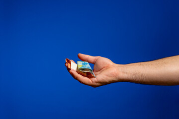 Man's hand offering folded euro bills on the palm of his hand, gesture of generosity. Isolated on blue studio background