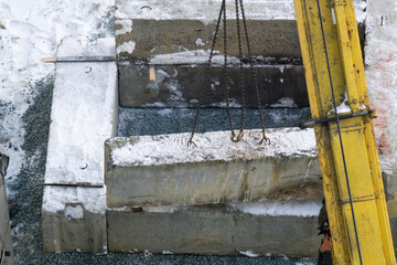 The crane manipulator assembles a foundation from concrete blocks. Construction site in winter. The crane moves the reinforced concrete block secured by the chains to the hooks.