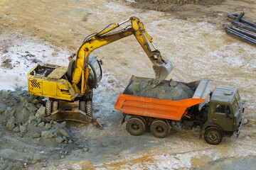 An excavator loads rubble into a truck, top view. Loading work at a construction site in winter. An excavator bucket pours gravel into the truck bed.