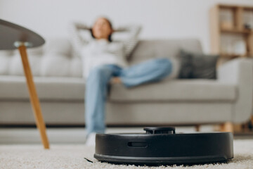 Woman relaxing while robot vacuum cleaner cleaning up the room