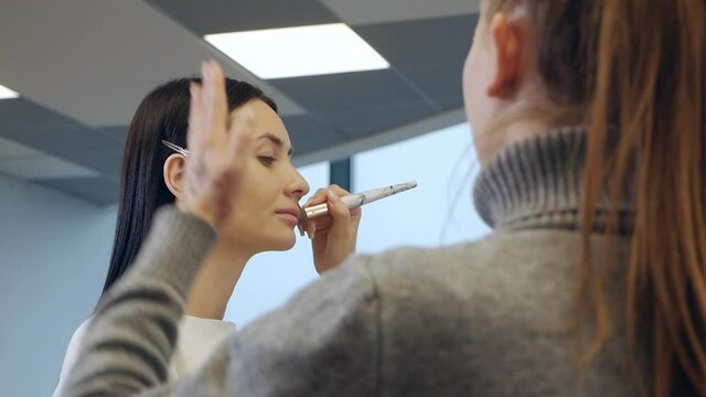 Makeup teacher with his student. Make-up lesson at beauty school. Master Class. The student does the makeup of the model under the supervision of a professional make-up artist