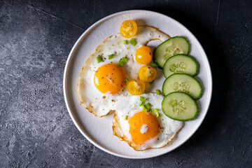 fried eggs with bacon on a white plate and gray background.