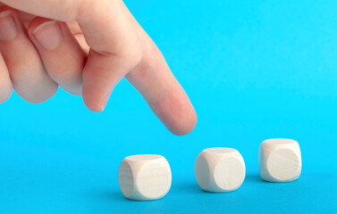 Finger pointing at one of three blank plain wooden blocks, group of cubes. Man choosing, selecting,...