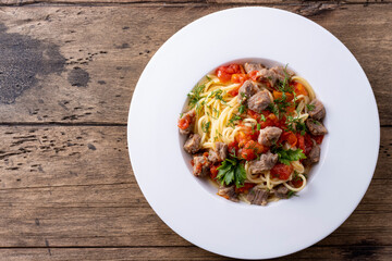 pasta with tomato sauce and meat on white plate and wooden background